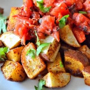 Close up view of spicy Mexican potatoes roasted and served on a white plate.