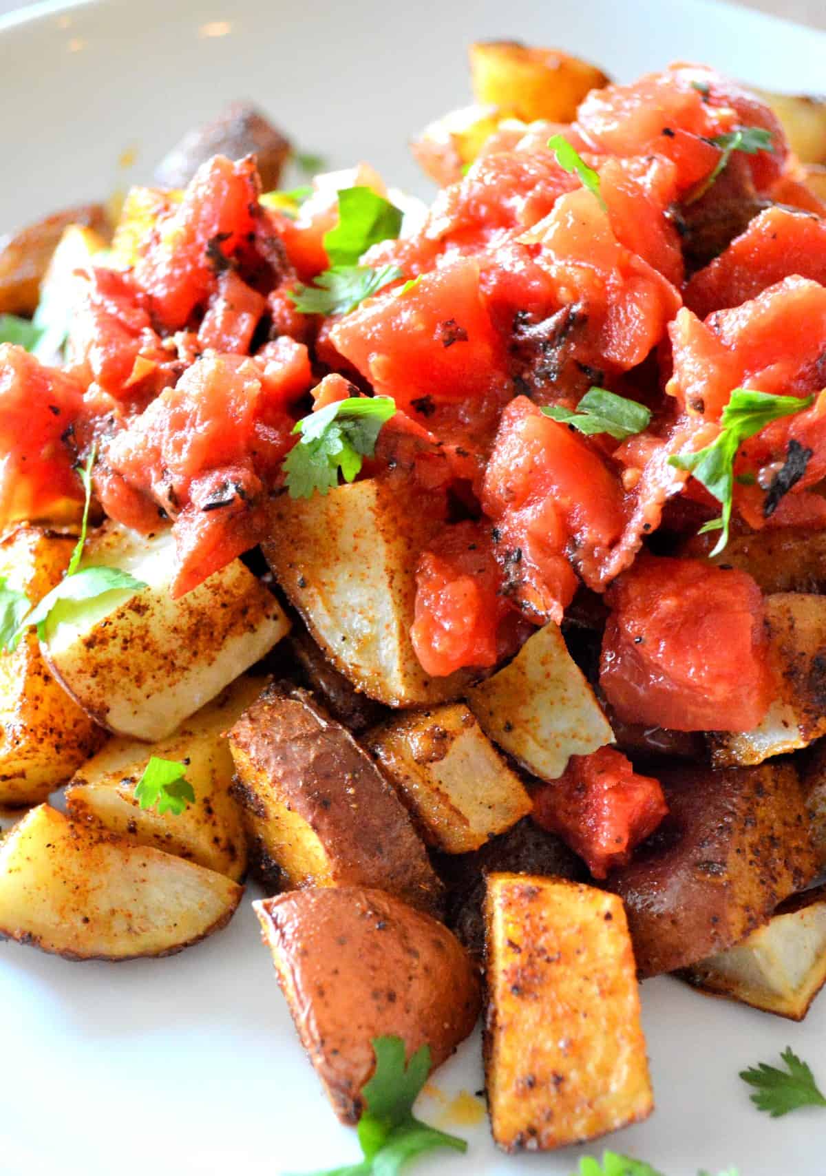 Close up view of a side dish mixed with roasted tomatoes and served on a plate with parsley as garnish.