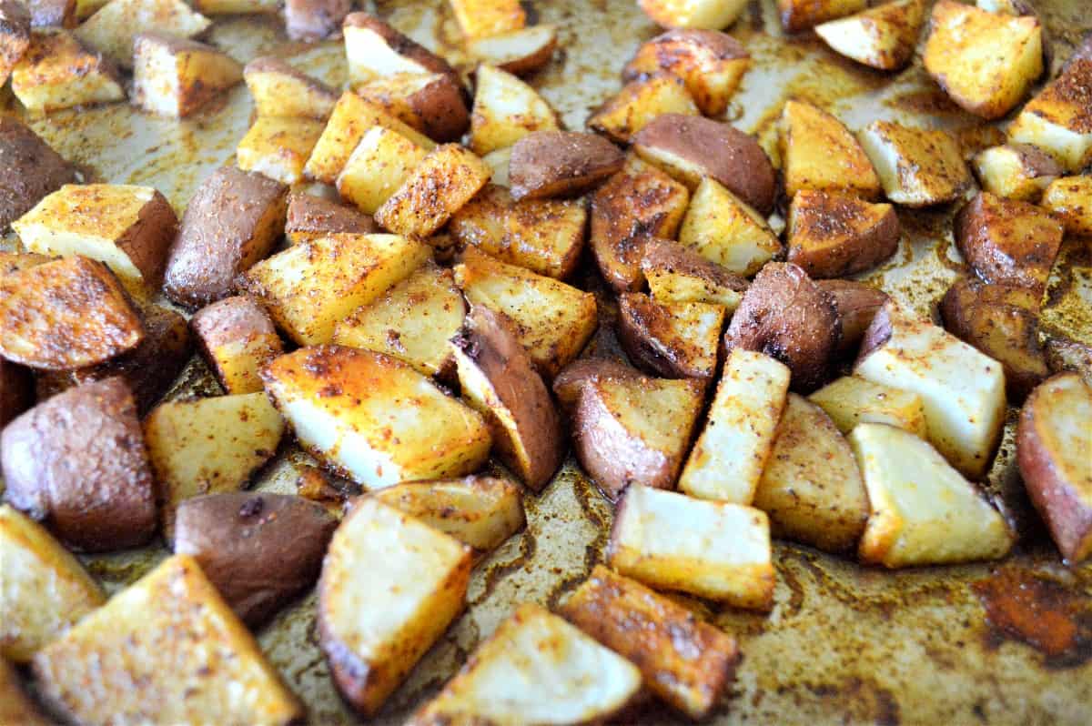 Wide photo of roasted red potatoes on a baking sheet ready to be scooped up.