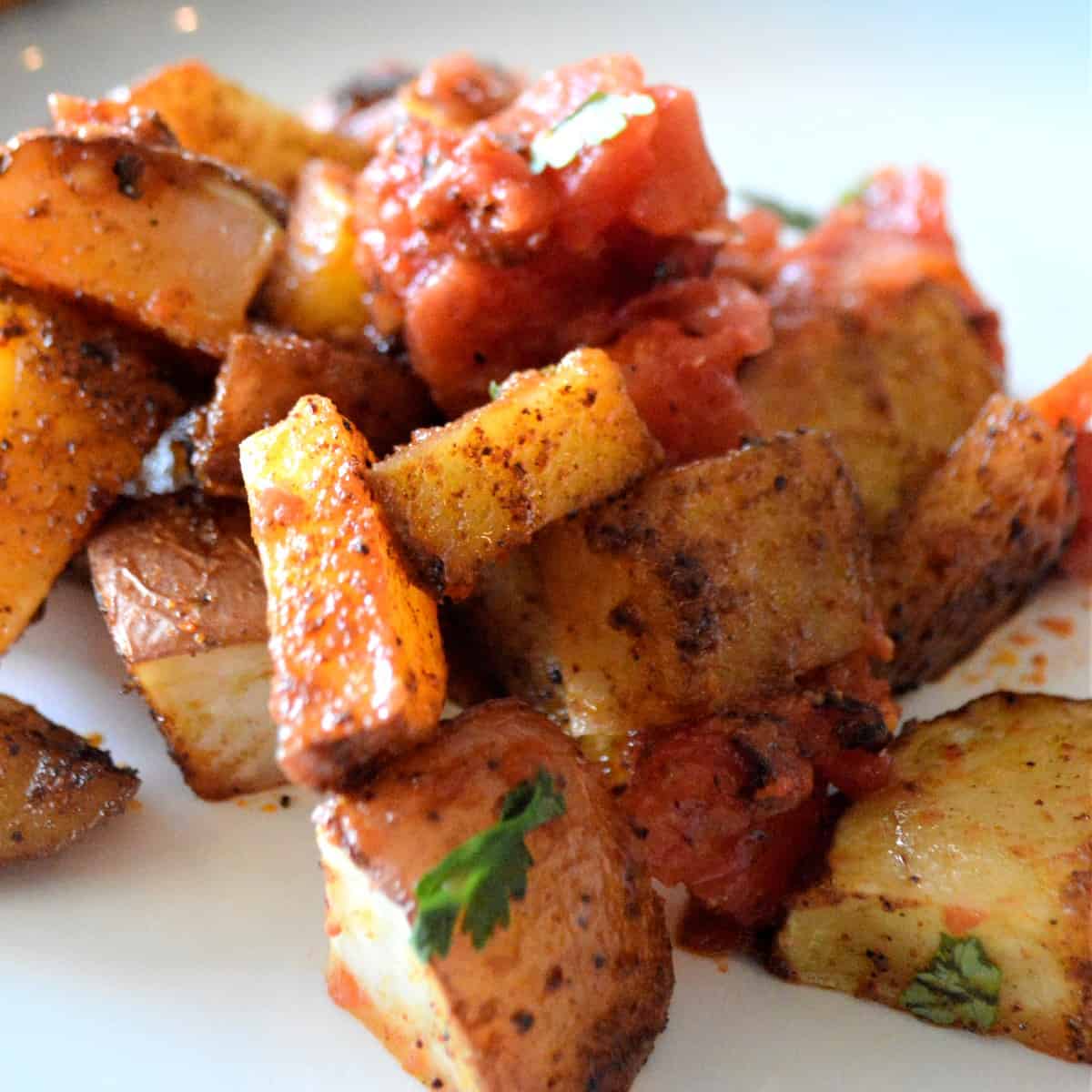 Close up square photo with potatoes and tomato topping piled on a small plate.