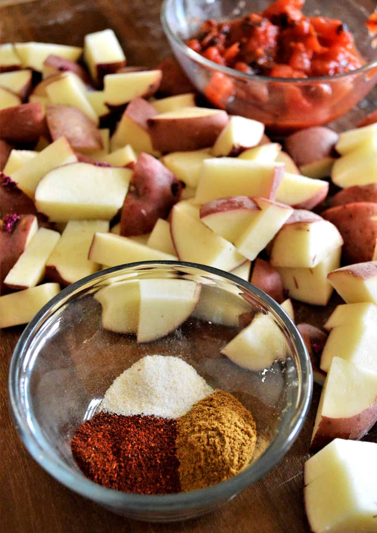 Cut red veggies in the background with a small bowl full of the recipes spices.