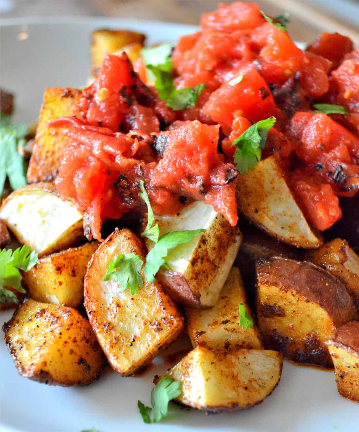 Roasted new potatoes served on a white plate with roasted tomatoes on top.