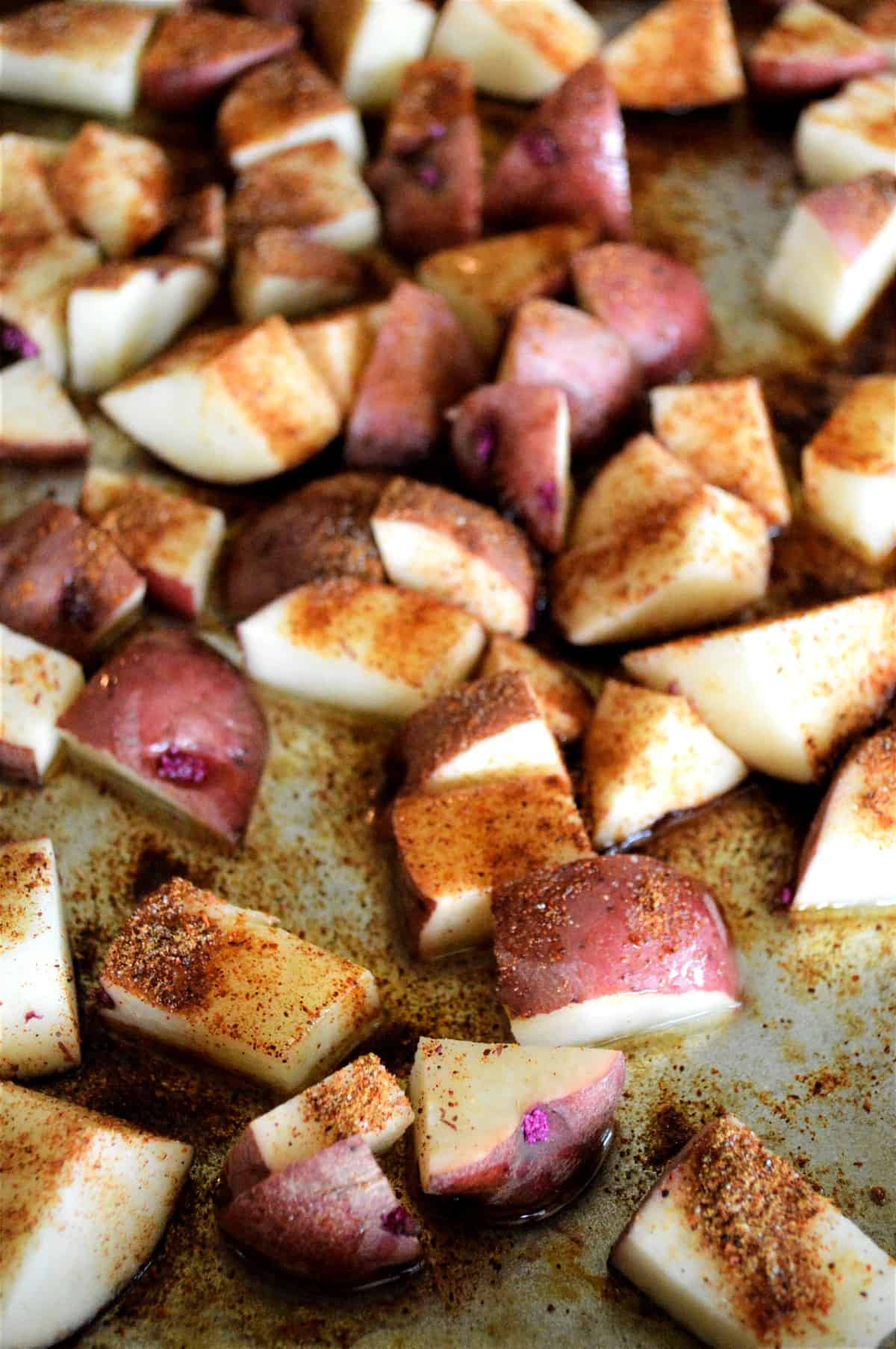 Cut and prepared vegetables mixed with spicy seasonings and spread out on a baking sheet before baking.