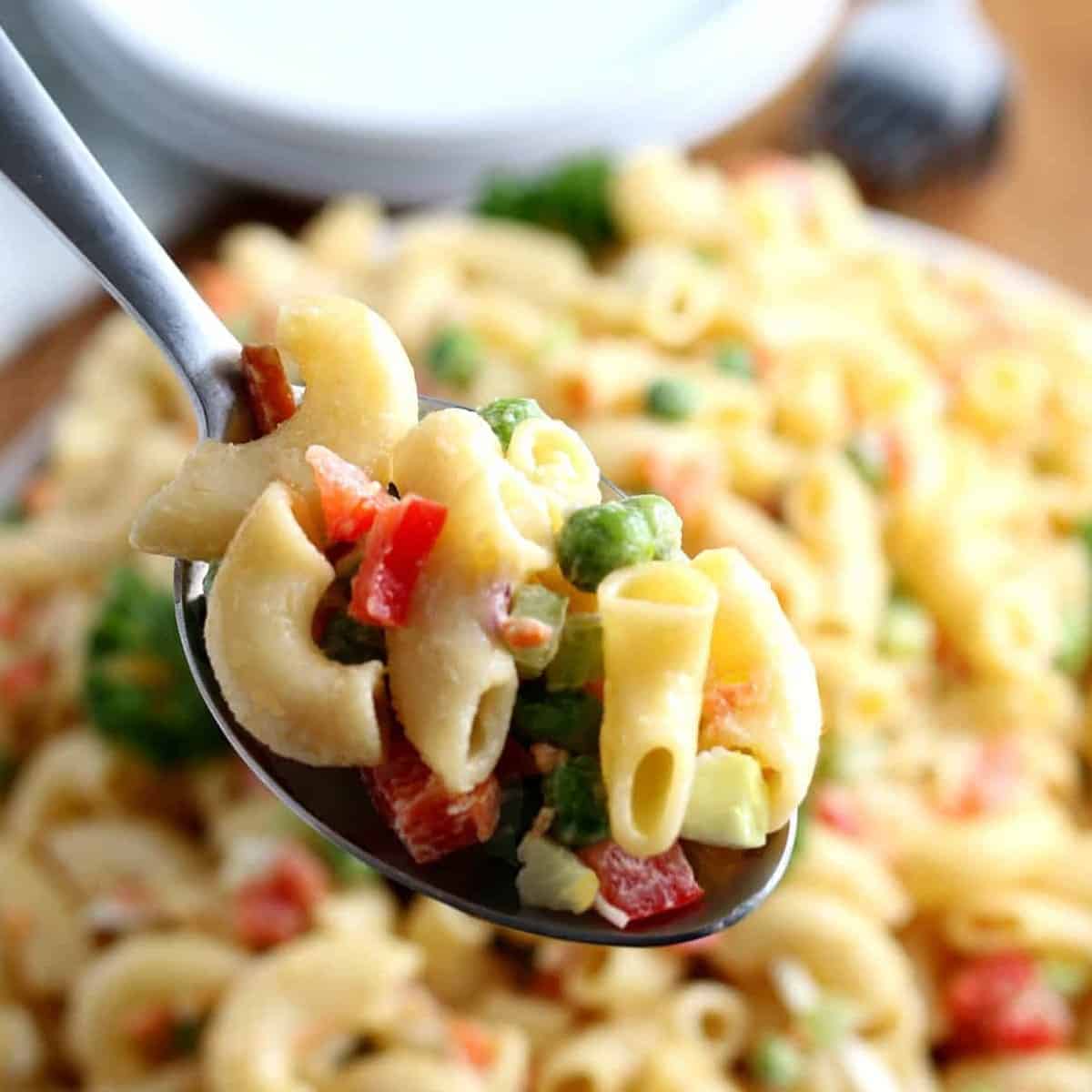 A very close up spoon that's filled with vegan macaroni salad. The bowl of pasta is blurred in the background.