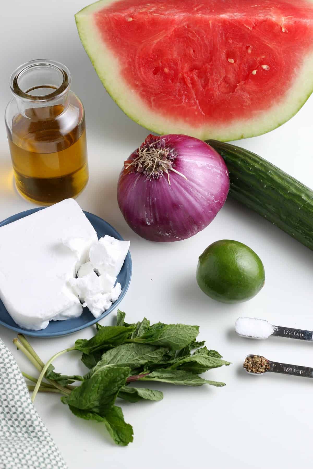 All of the ingredients for a watermelon salad against a white background. Nothing is prepped yet.