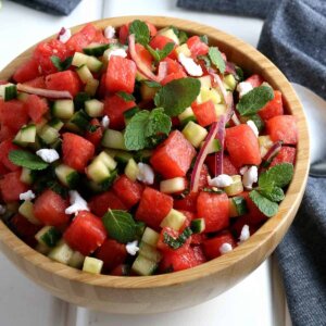 Tilted wooden bowl filled with watermelon feta salad with fresh mint and vegan feta.