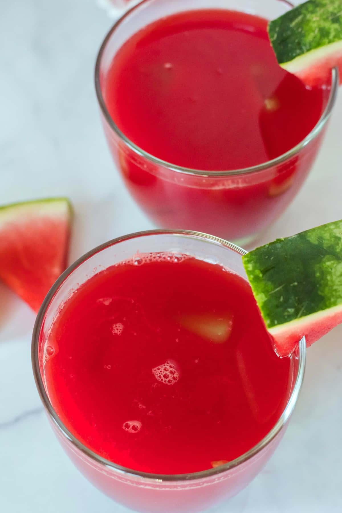 Looking down at two glasses filled with a red drink and they both have a small fruit wedge as garnish.