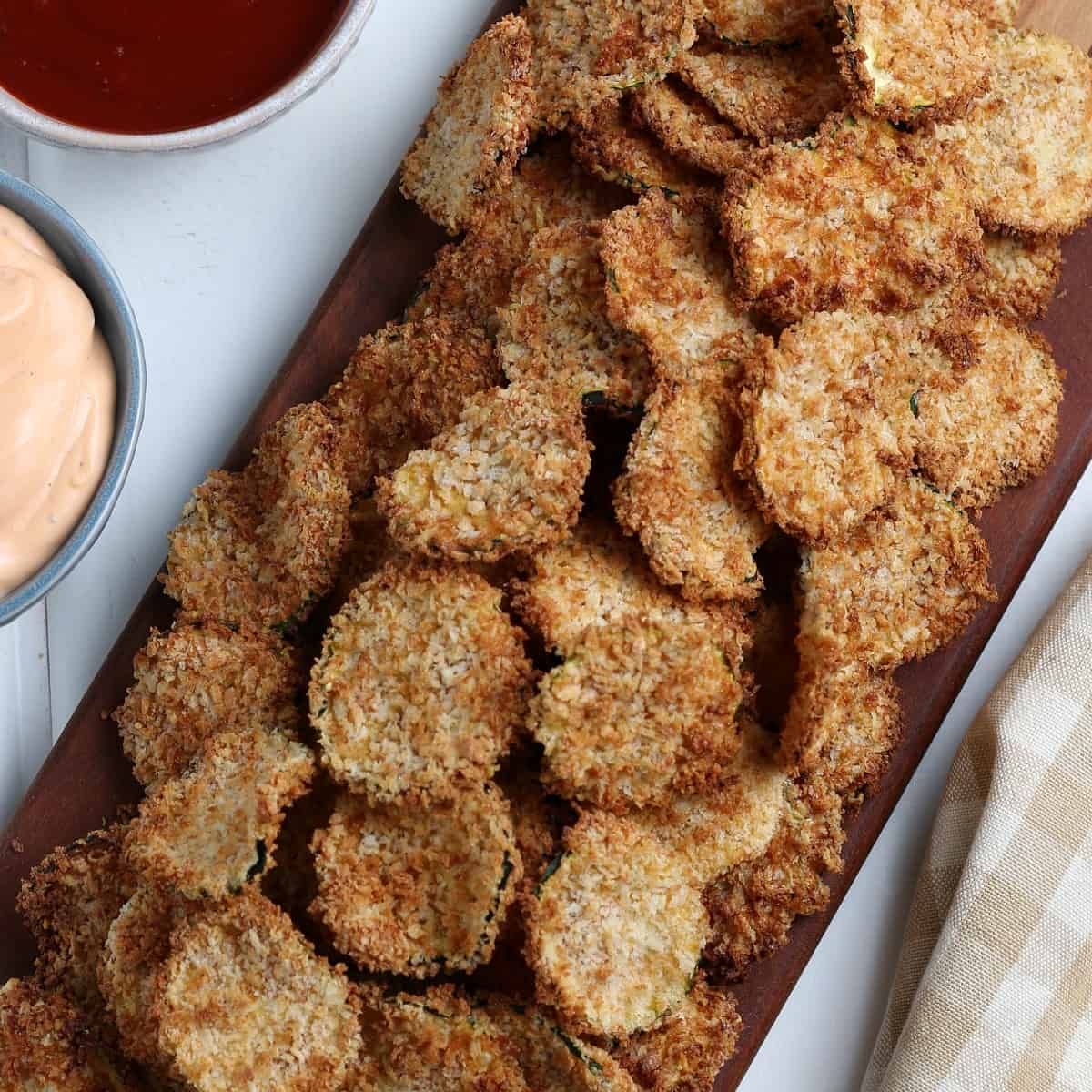 Overhead view of a pile of golden zucchini chips on a wooden tray.