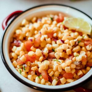 Close up bowl of chipotle corn salsa showing dice tomatoes and lime on the side.