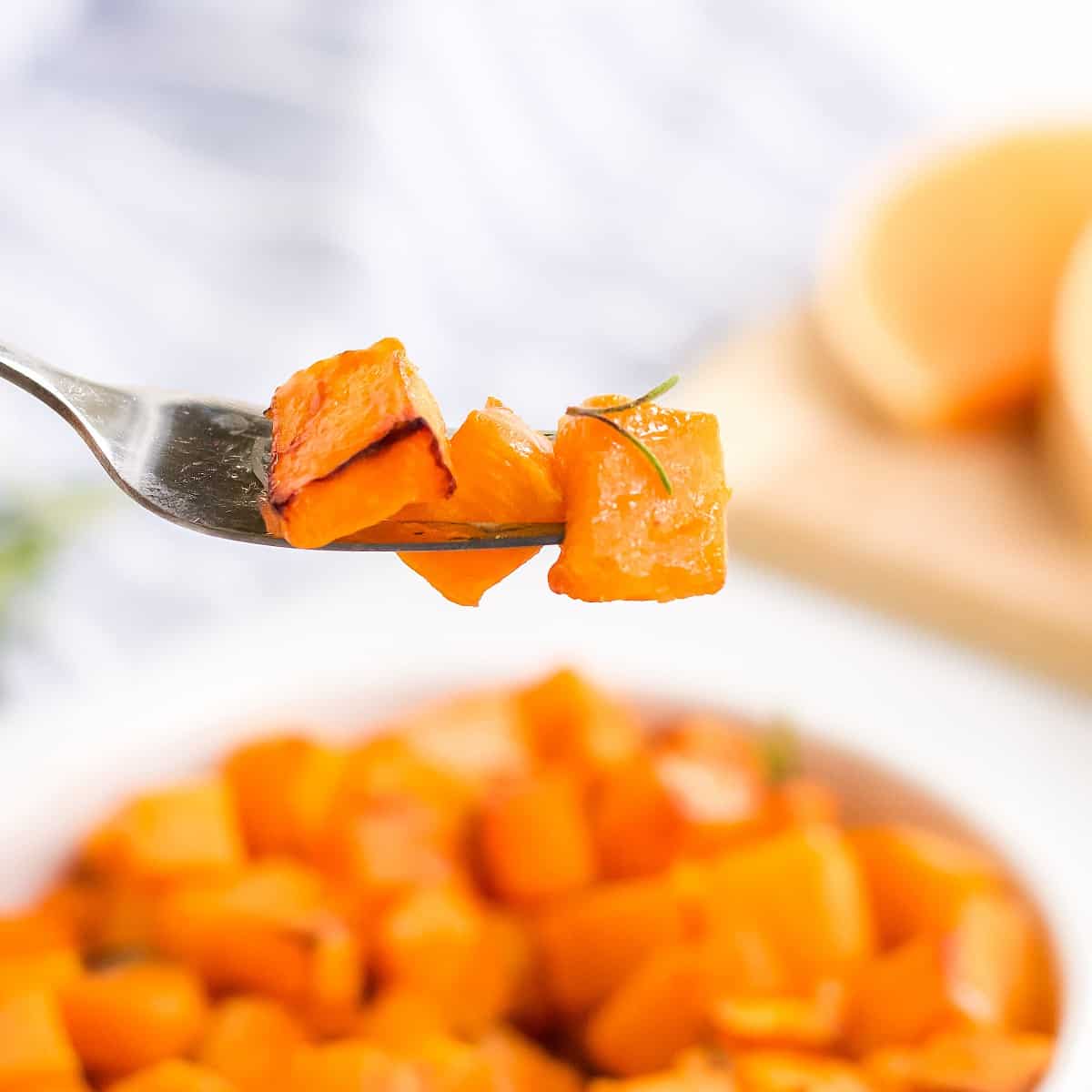 A forkful of butternut squash is help close to the camera lens.