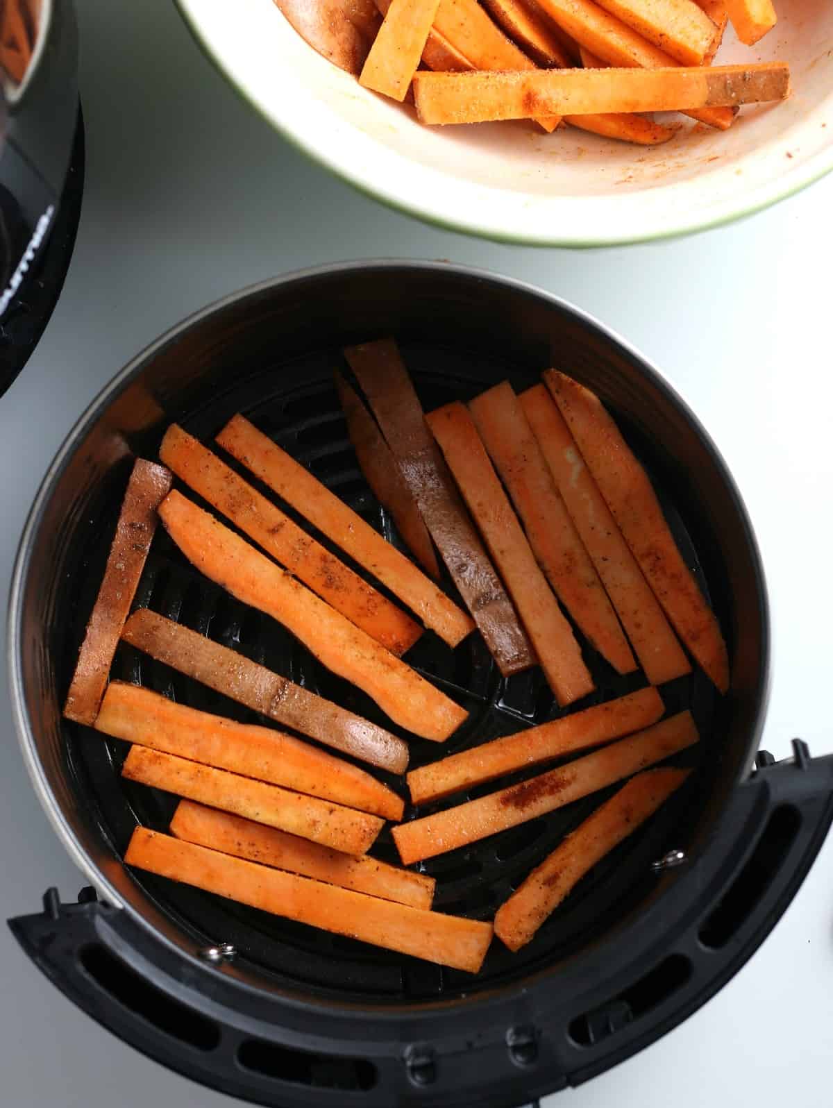 Raw sweet potato matchsticks laying in the bottom of an air fryer.