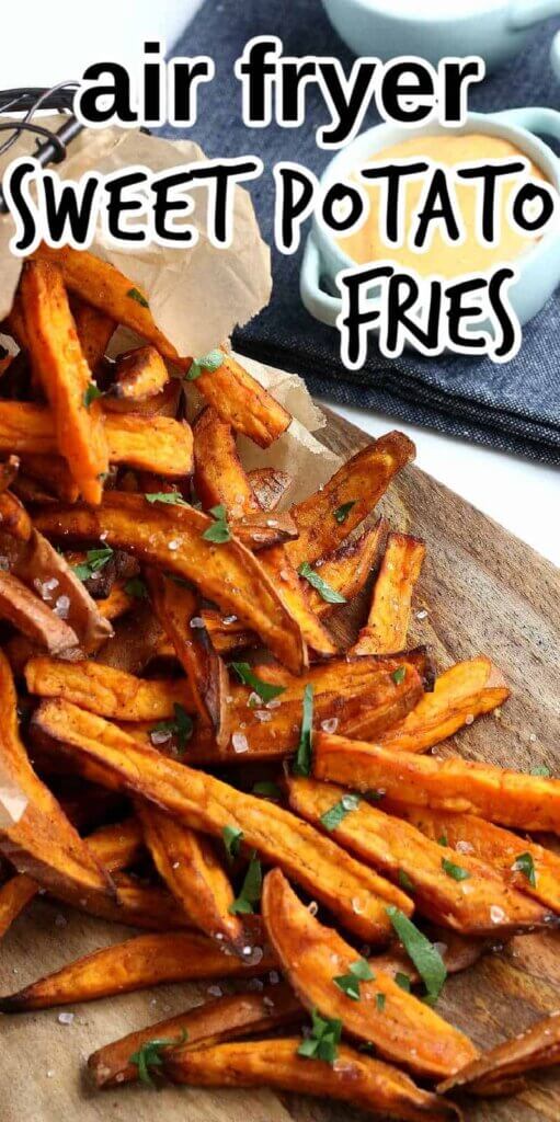 Sweet Potato Fries are spilling out onto a wooden board with dipping sauce.