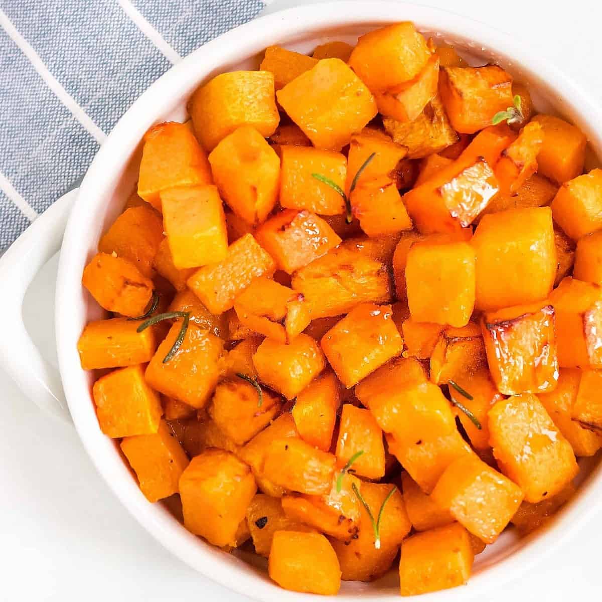 Overhead view of cooked cubed butternut squash in a white bowl.