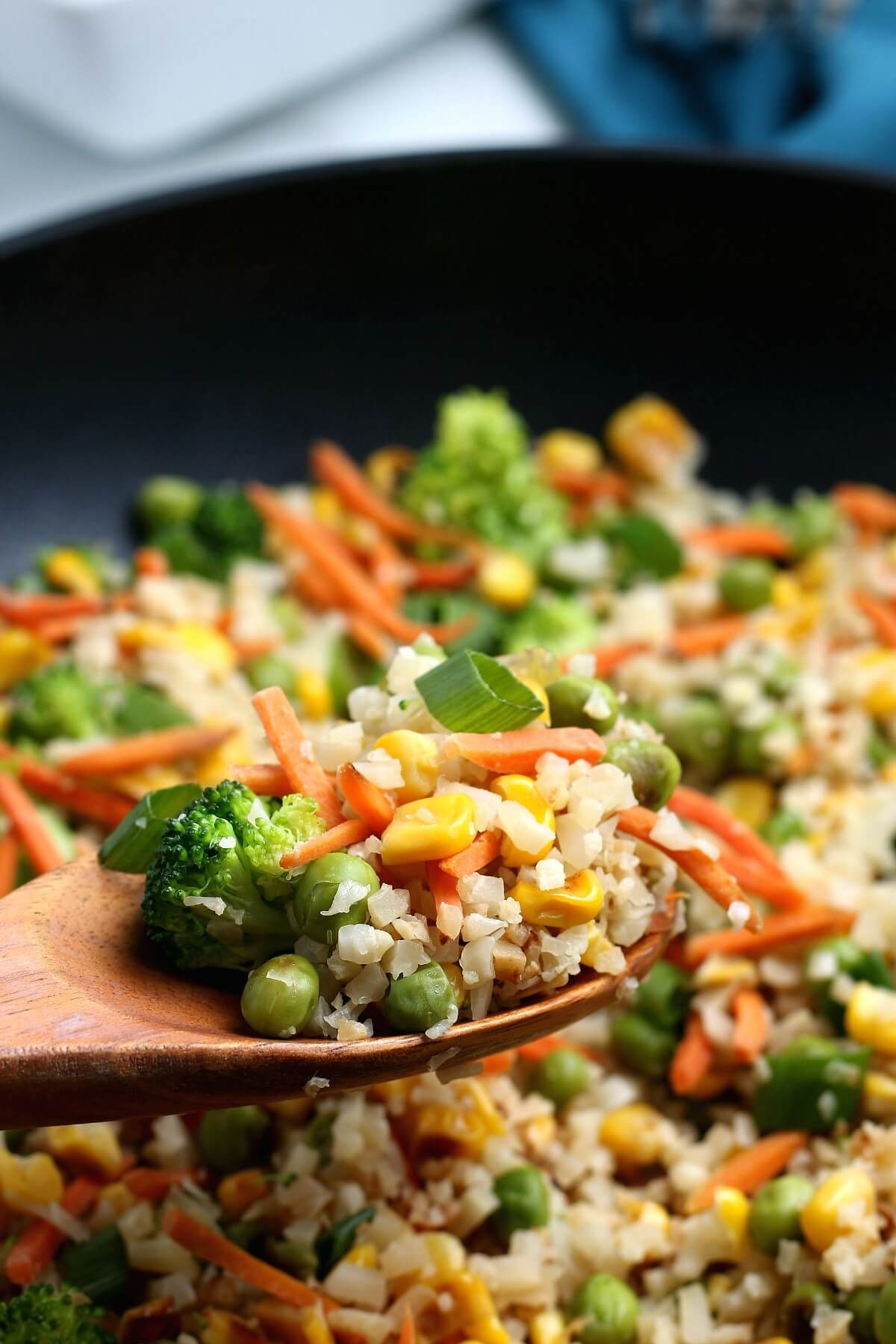 A wooden spoon with a scoop of mixed veggies being held close to the camera.