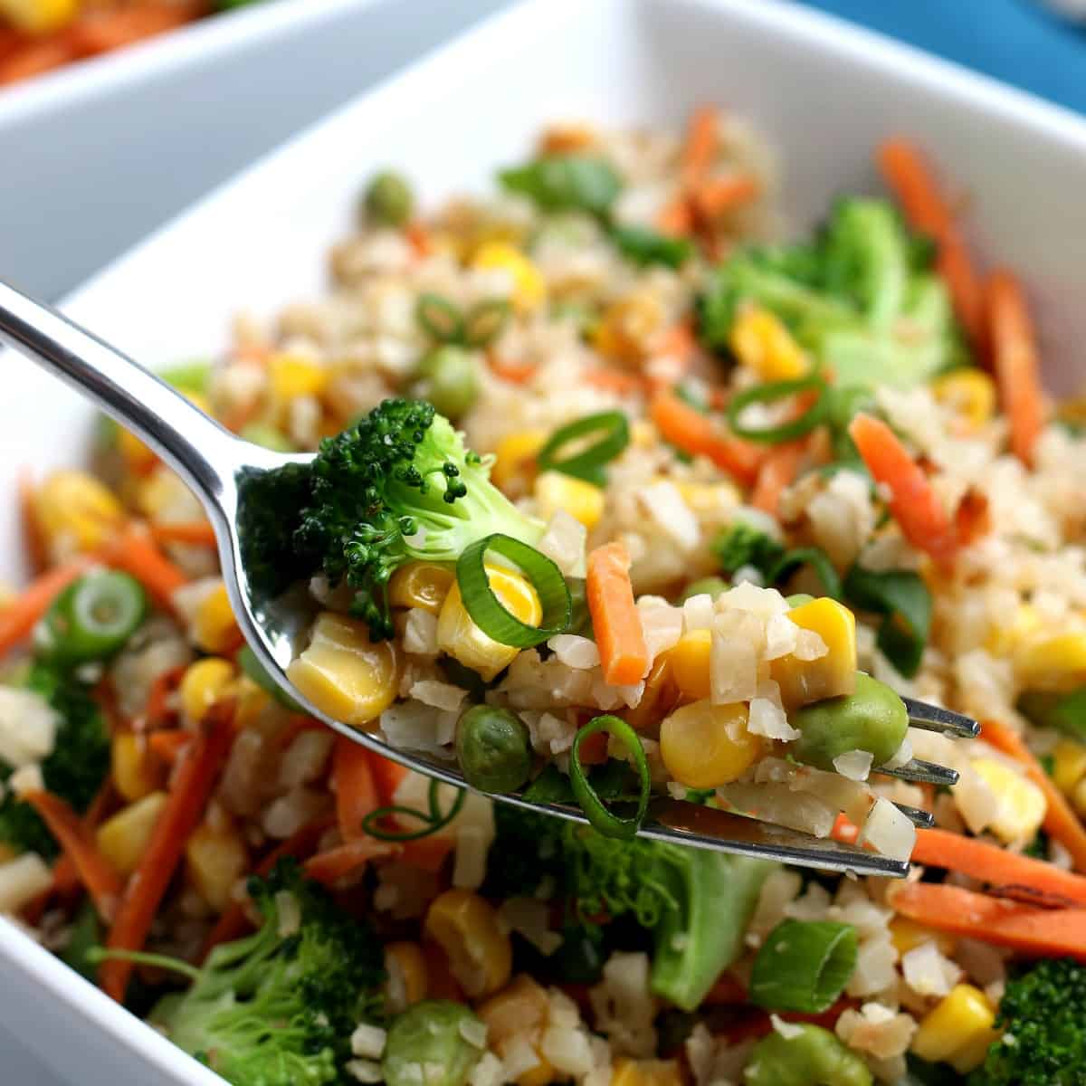 A fork full of mixed veggies is lifted up to the camera lens.