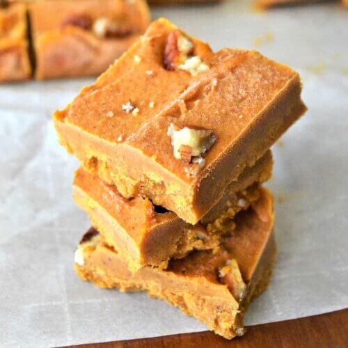 Three squares of pumpkin fudge stacked on top of each other on parchment paper.