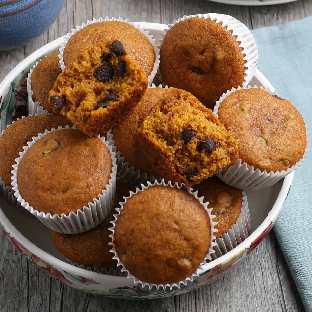 Pumpkin chocolate chip muffins in paper cups and a flowered bowl.