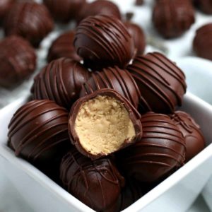 A pile of chocolate covered peanut butter truffles in a white bowl.