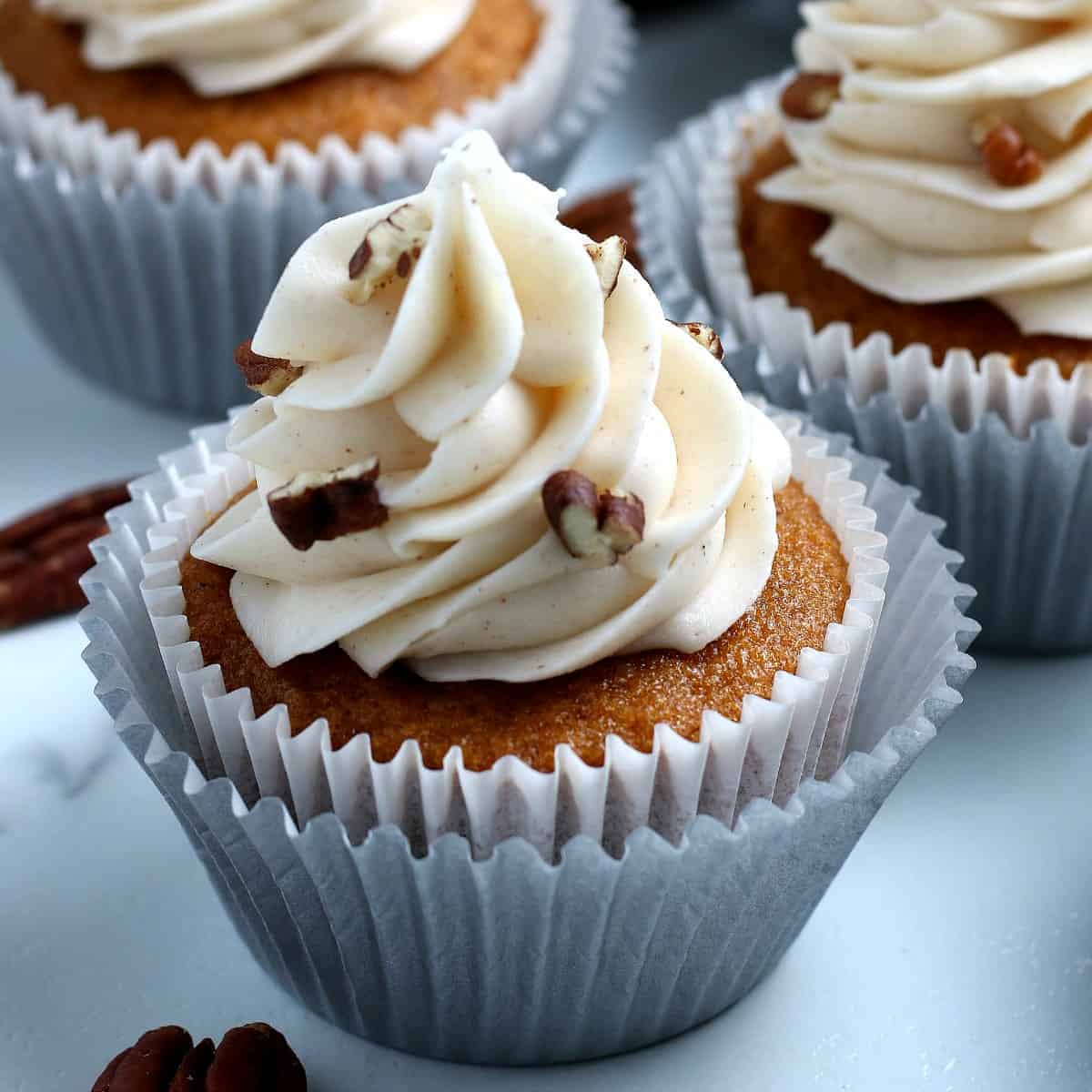 One closeup of a pumpkin cupcake topped with a swirl of cream cheese frosting.