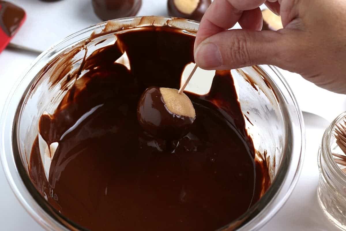 Partially dipping a peanut butter ball into melted chocolate.