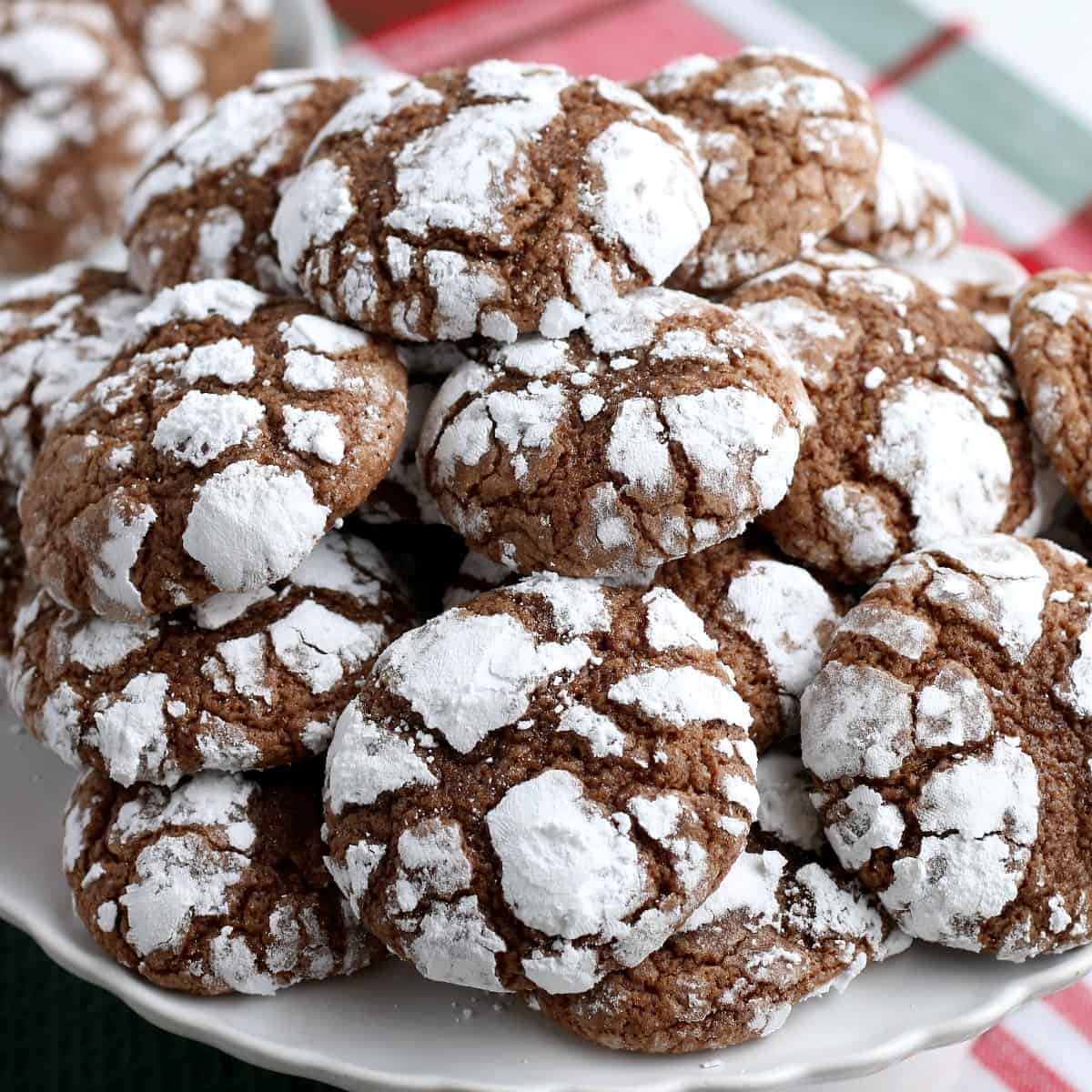 Closeup of chocolate crackled cookies piled on a white plate.