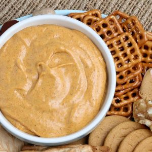 Overhead cropped bowl of pumpkin dip with cookies and nuts scattered around,