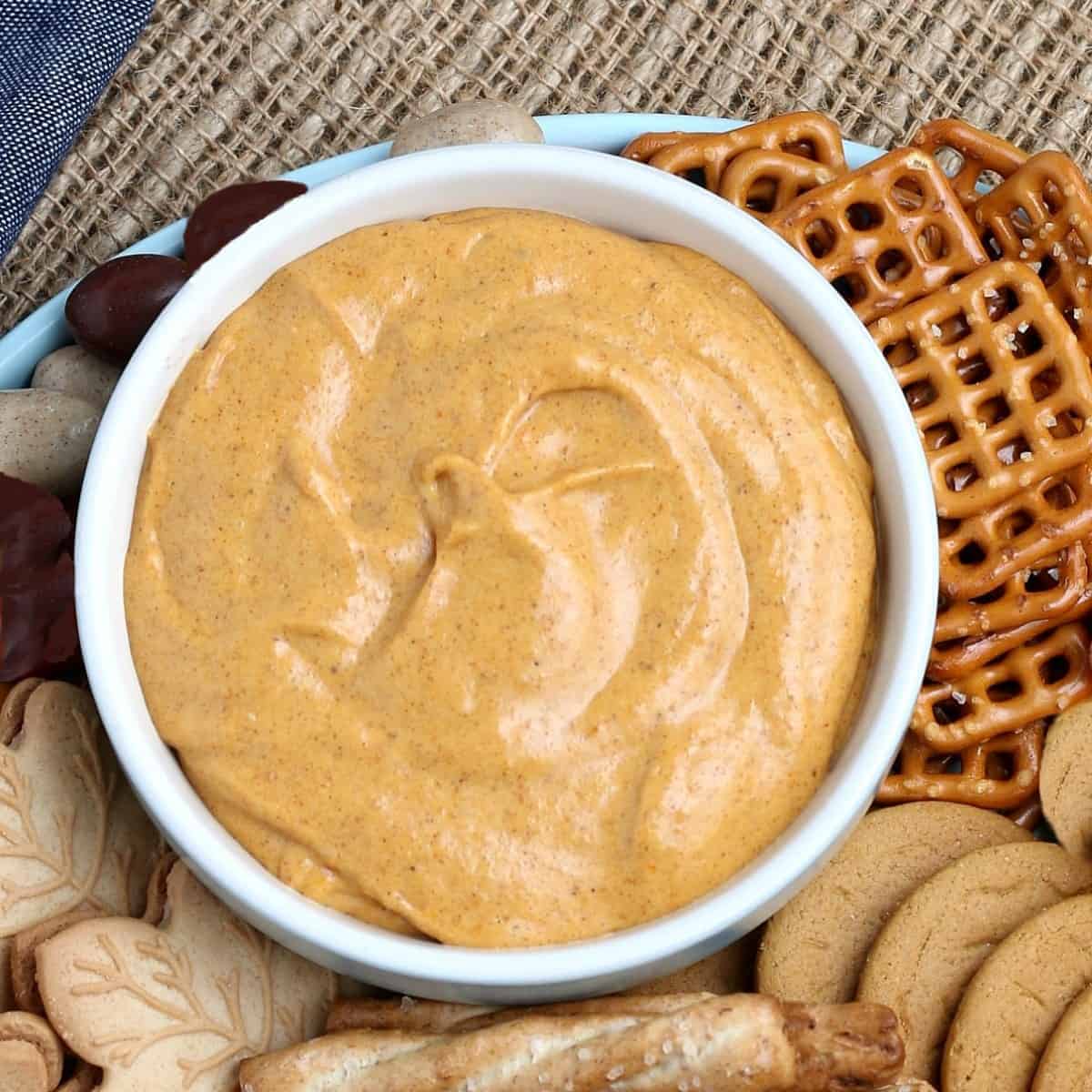 Overhead centerd bowl of pumpkin dip with cookies and nuts scattered around,