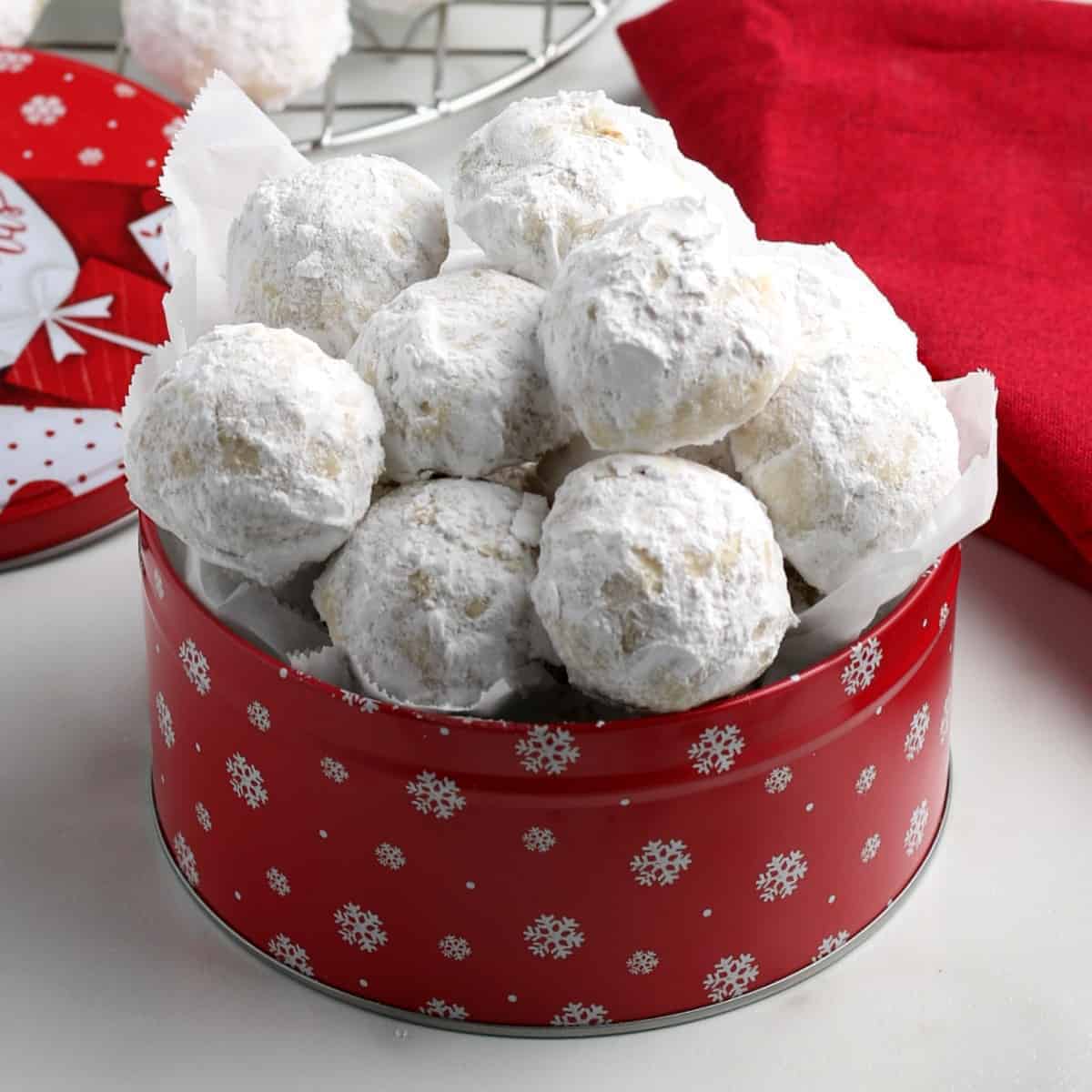 Red tin full of vegan snowball cookies which are covered in powdered sugar.