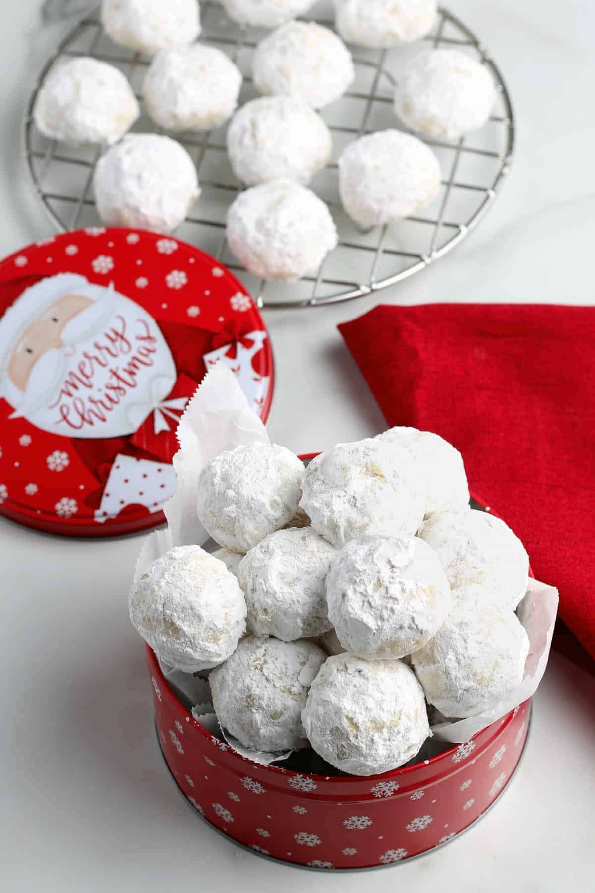 Powdered sugar covered vegan snowball cookies in a red tin and on a cooling rack.