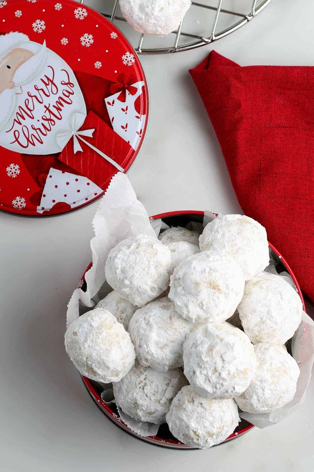 Overhead photo of a tin full of vegan snowball cookies with the lid on the side.