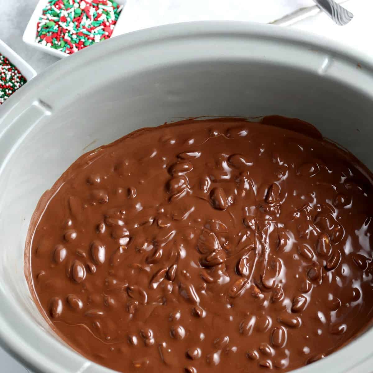 Looking into a slow cooker are the melted chocolate and peanut candy concoction.