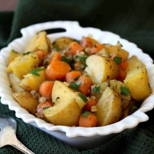 One photos showing a white scalloped bowl filled with cooked potato and carrot chunks.