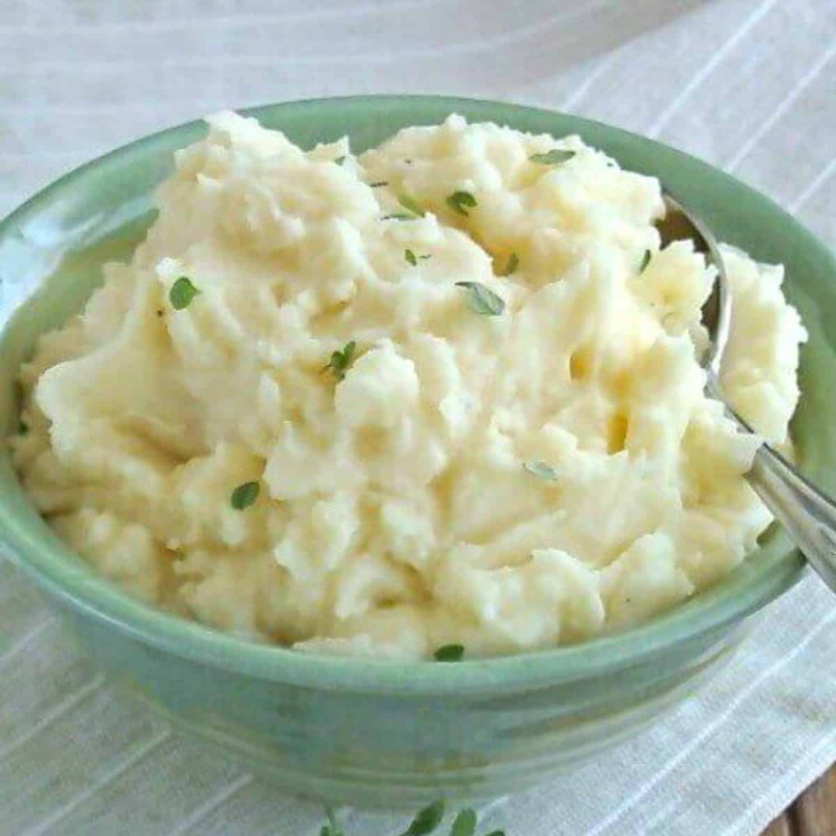 Crock pot mashed potatoes are in a green bowl with thyme sprinkled on top.