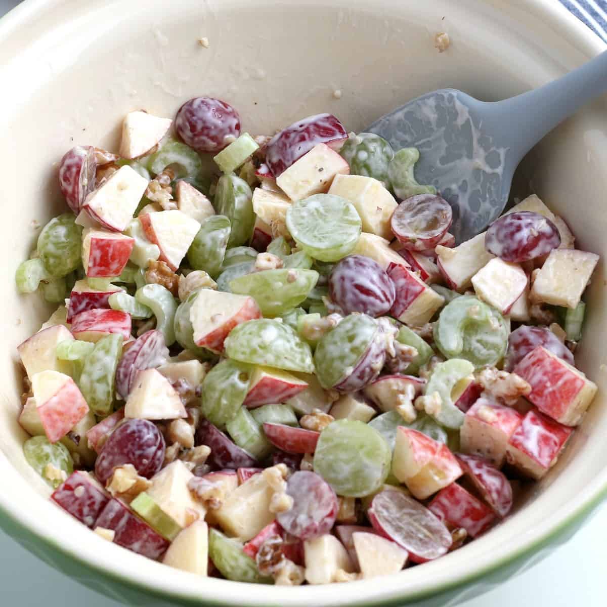 A mixing bowl full of tossed fruits, vegetables and salad dressing.