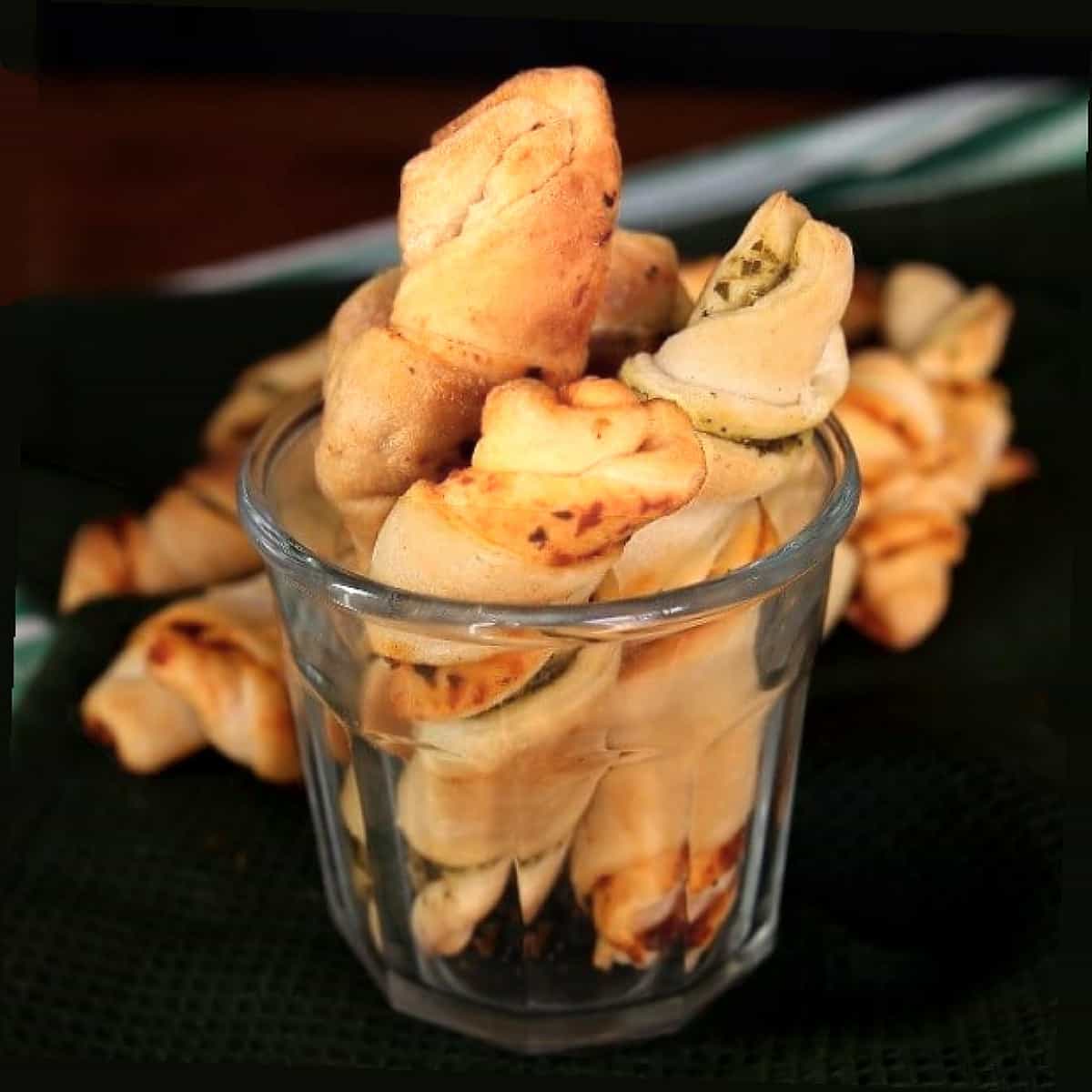 Rolled up crescent roll appetizers sticking out of a wide mouth glass.