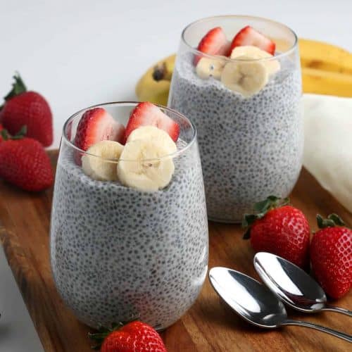 Two glasses are filled with chia seed pudding and they are topped with fresh fruit.