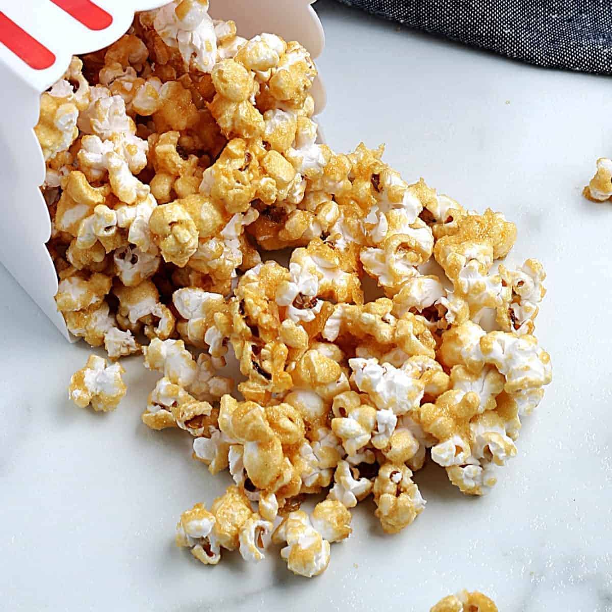 Caramel popcorn spilled out onto a white table from a popcorn box.