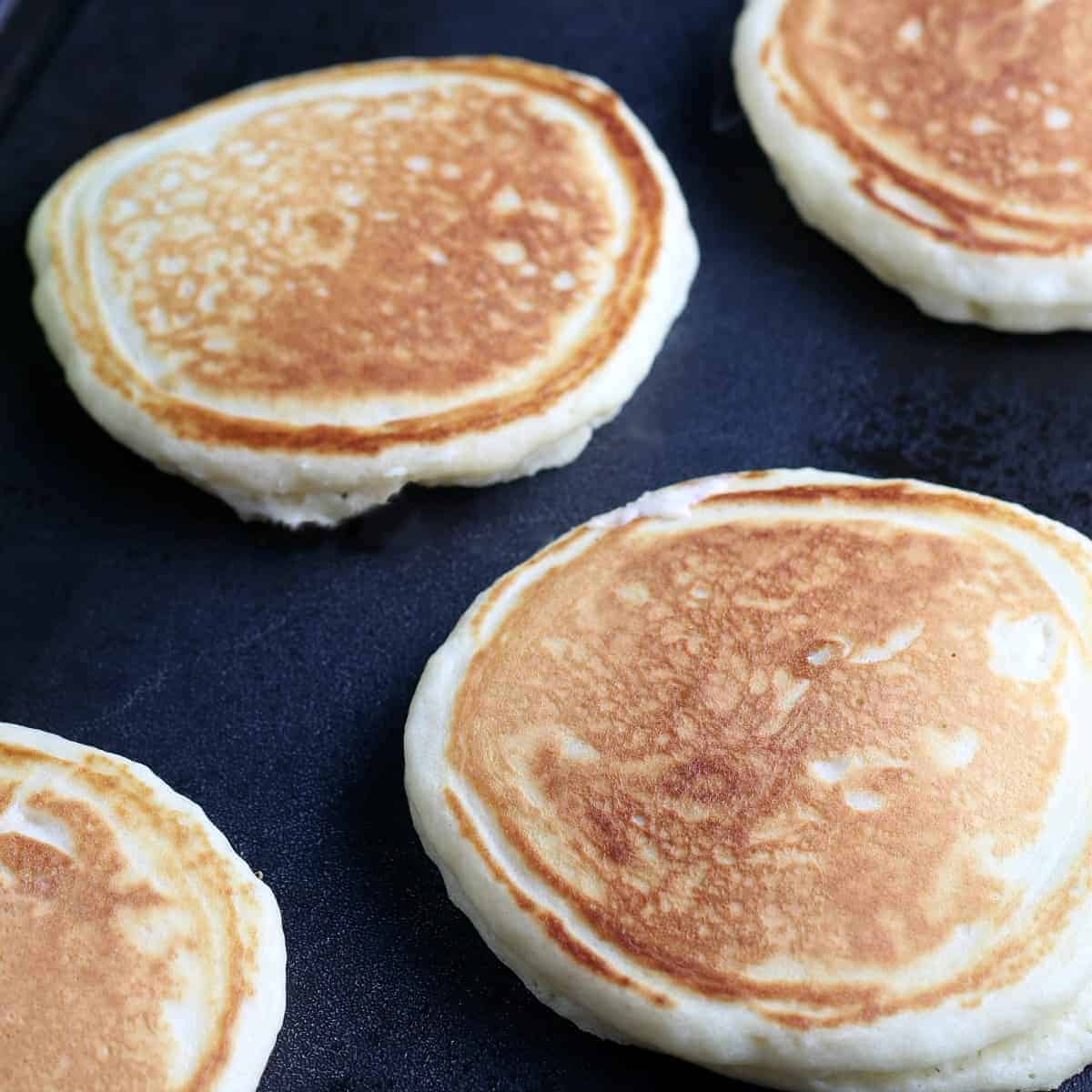 Close up of golden pancakes flipped on a griddle.