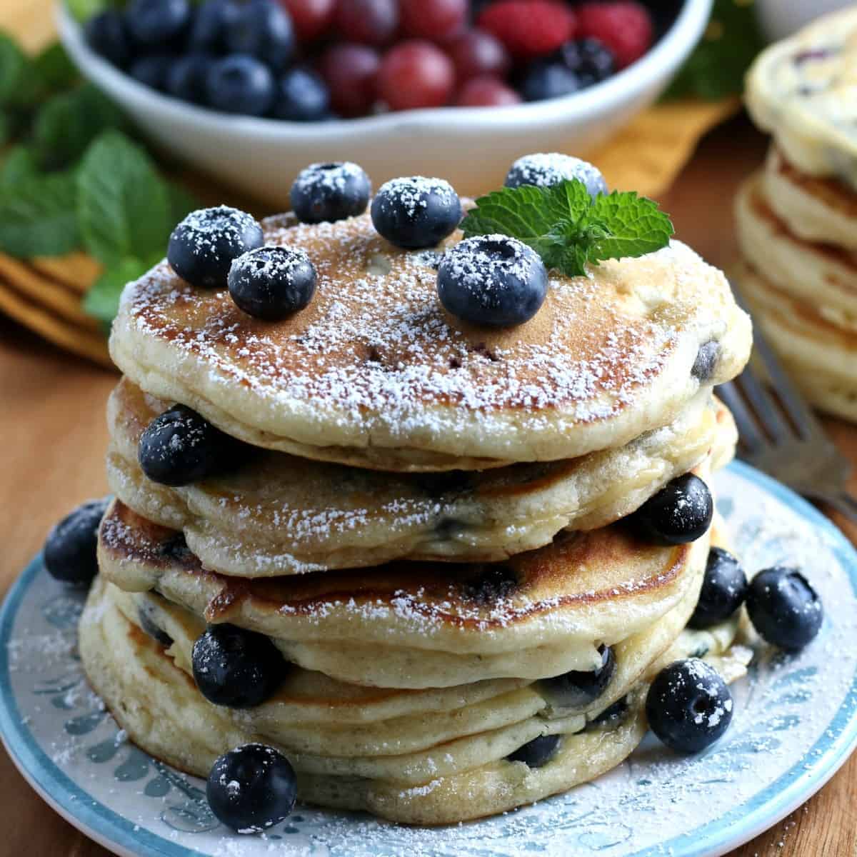 Stack of four pancakes showing blueberries and sprinkled with powdered sugar.