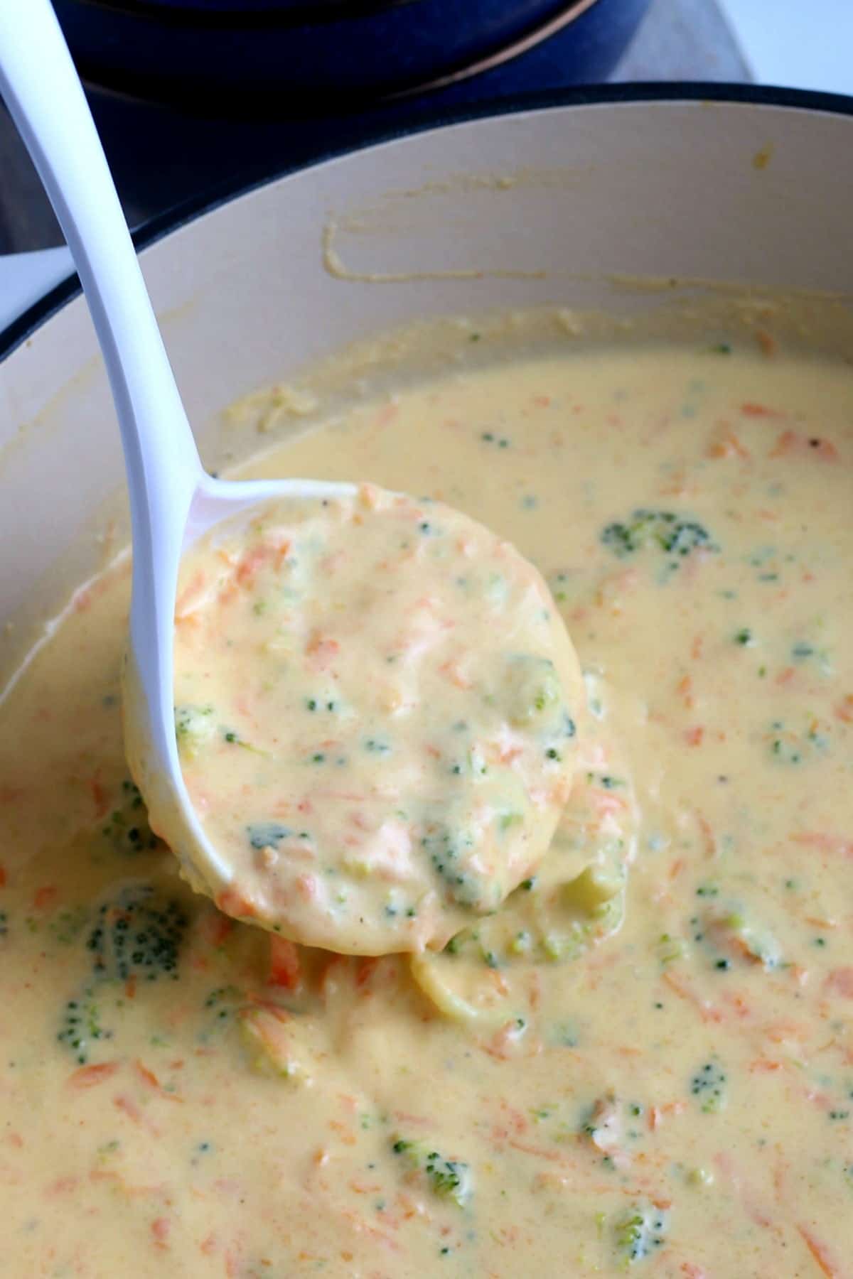 Close up of a ladle full of a creamy broccoli cheese soup recipe.