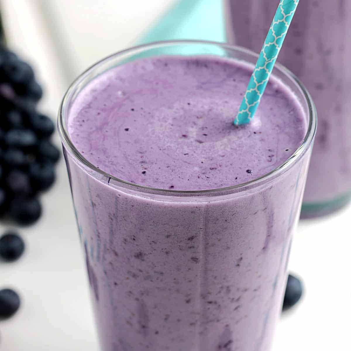 Titled glass full of blueberry protein shake and a straw.