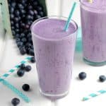 Glasses with fruit smoothie with fresh blueberries behind.