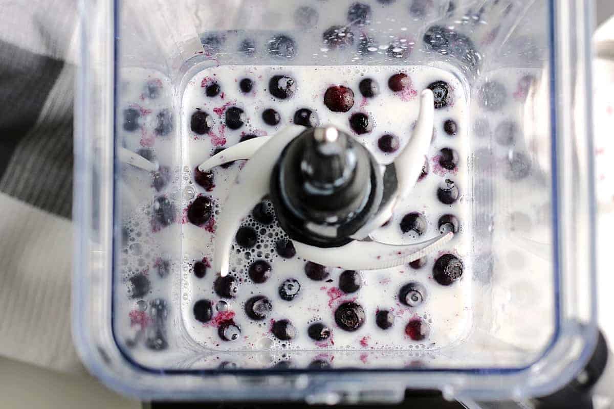 Looking down in to a blender at blueberries and dairy free milk.