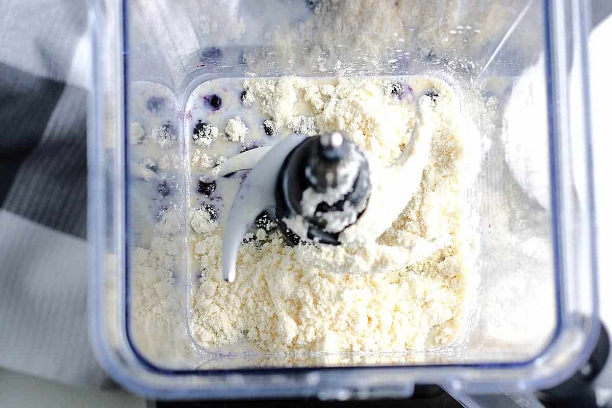 Looking down into a blender with protein powder on blueberries and milk.