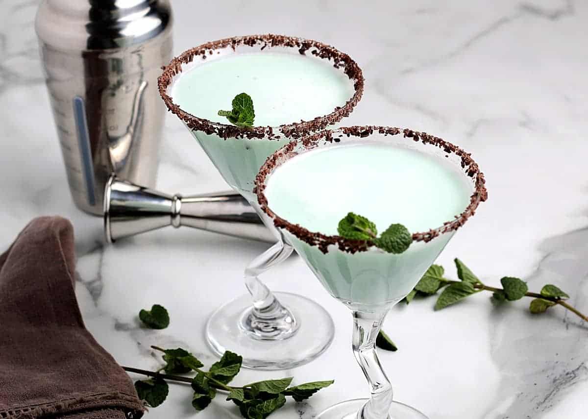 Wide photo of two martini glasses filled with a pale green and frothy cocktail.