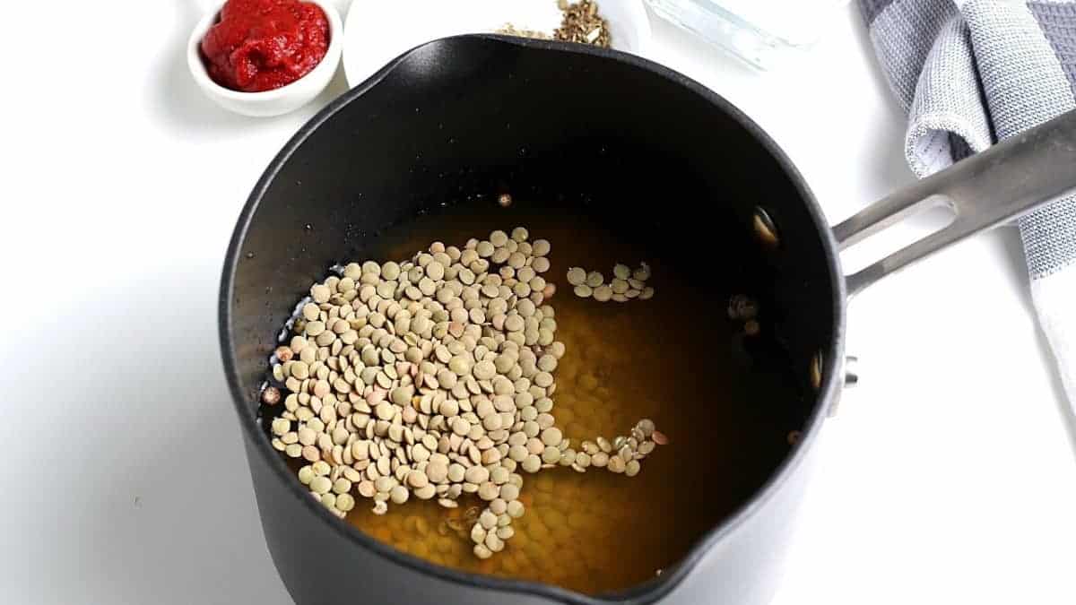 Saucepan filled with broth and lentils ready to be cooked.