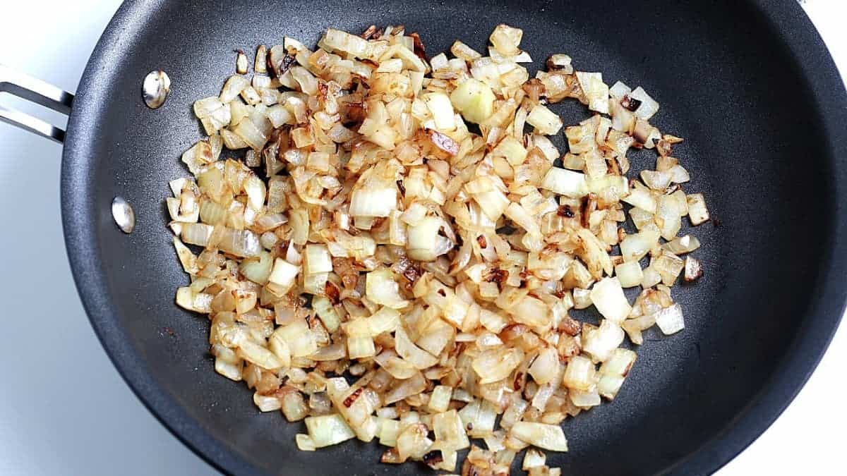 Overhead view of sauteed onions in a frying pan to start the vegan hash.