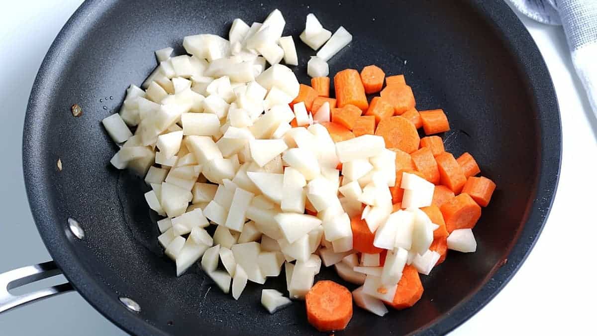 Overhead view of raw carrots and potatoes added to a frying pan.