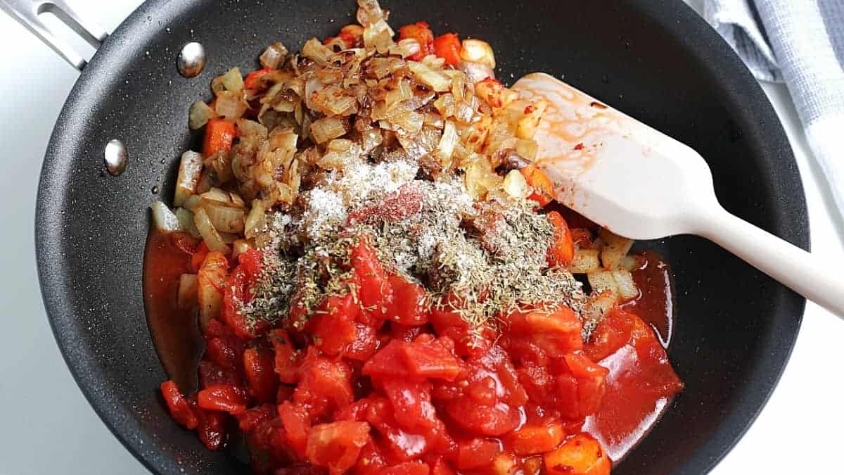 A skillet with added tomatoes, herbs and onions on top of the potatoes.