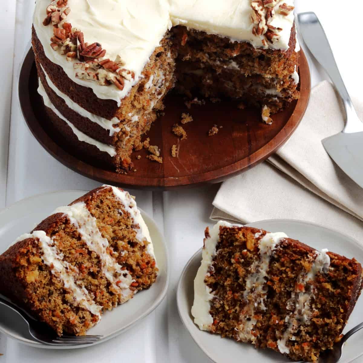 Two dessert plates with carrot cake slices and the three layered cake behind.